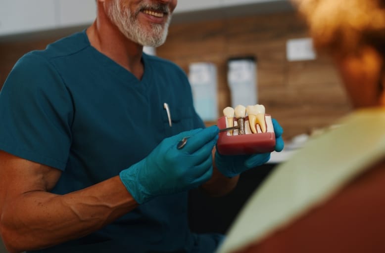 Dentist explaining dental implant procedure to patient using tooth model in Butler clinic